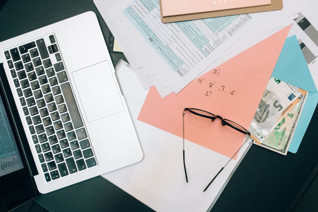 Bureau rangé avec un ordinateur portable ouvert, des documents papier et une paire de lunettes
