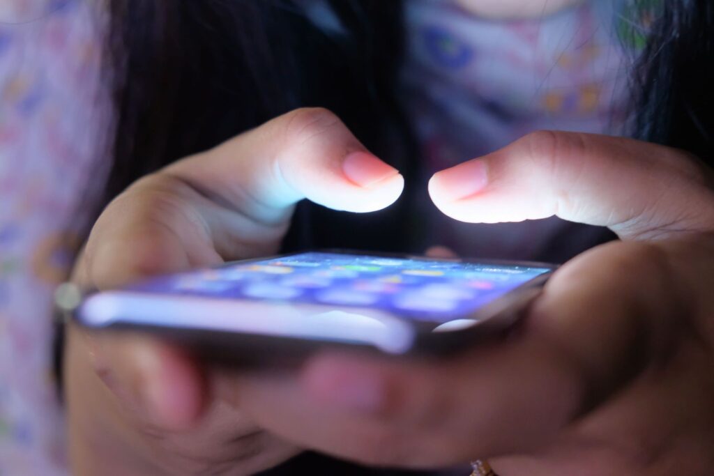 Mains tenant un smartphone à l'écran lumineux dans une pièce faiblement éclairée