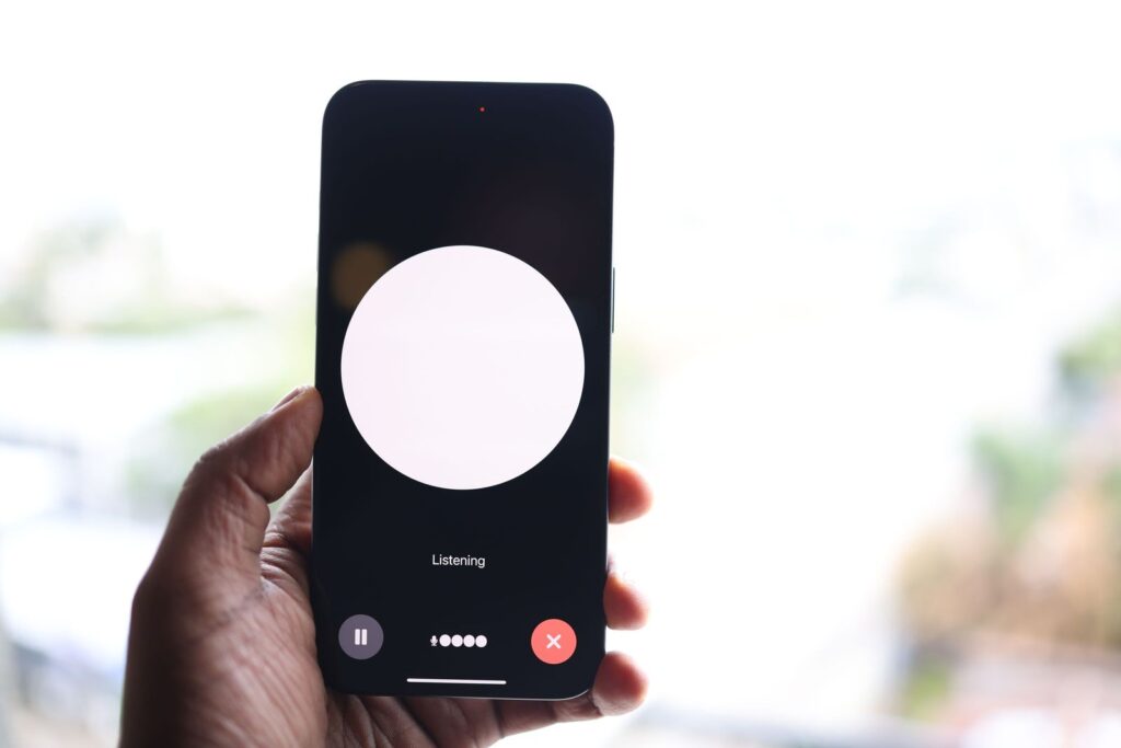 Main tenant un smartphone affichant l'interface d'un assistant vocal à l'écran