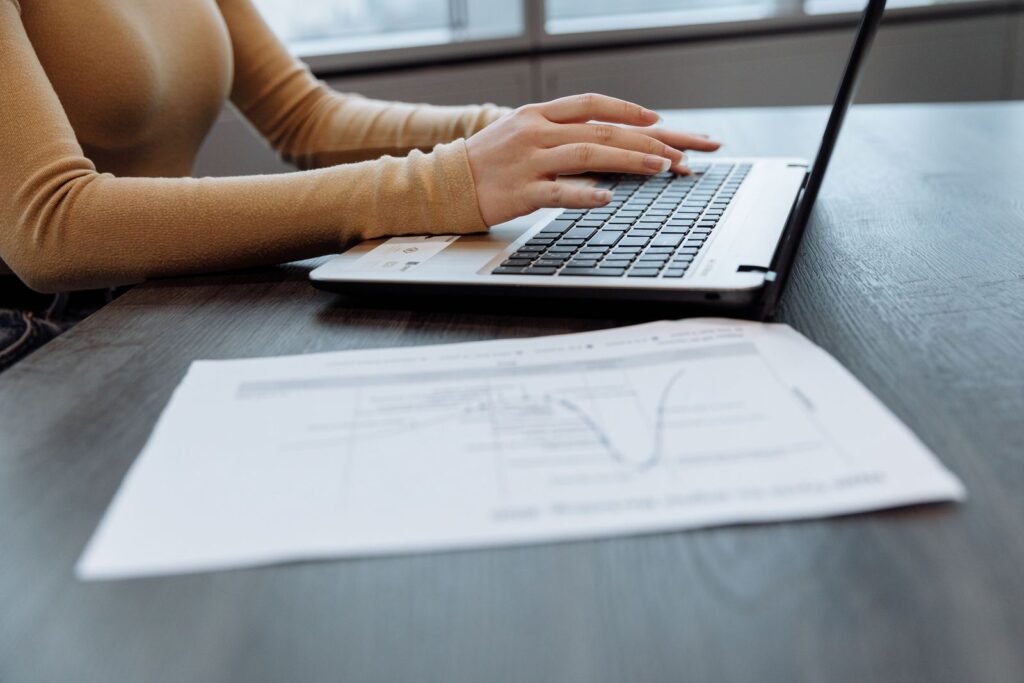 Mains tapant sur le clavier d'un ordinateur portable posé sur un bureau, à côté de documents